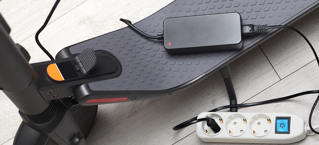 Cargador de un patinete enchufado y apoyado sobre él
