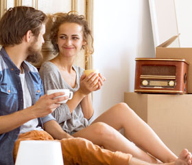 Pareja relajada tomando café y sentada en el suelo con cajas